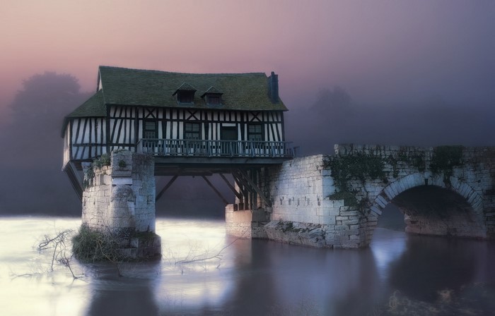 Half-timbered house on a stone bridge over a river at dusk