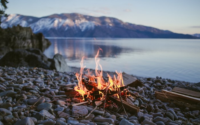 Campfire on a rocky shore with snow-capped mountains