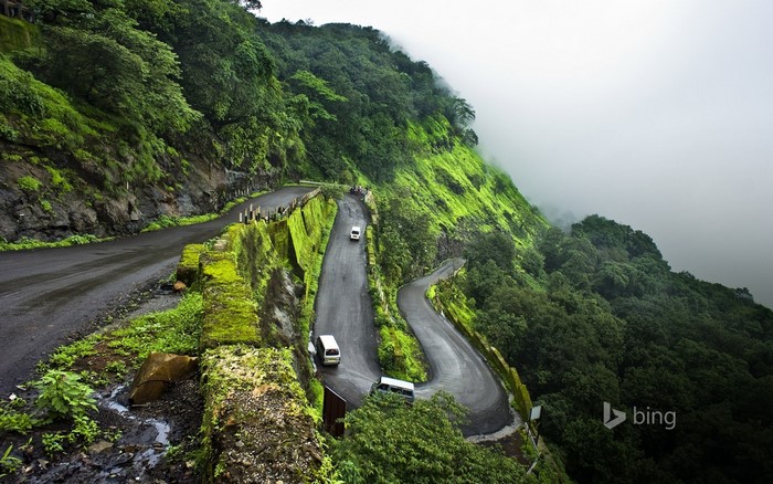 Winding mountain road through a lush green landscape with fog