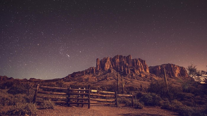Desert mountains under a starry night sky with a wooden fence