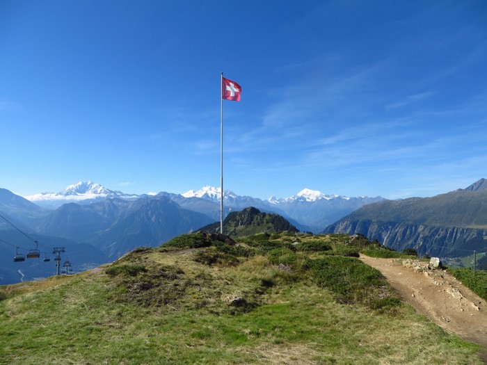 Swiss flag on a mountain peak with Alps in the background
