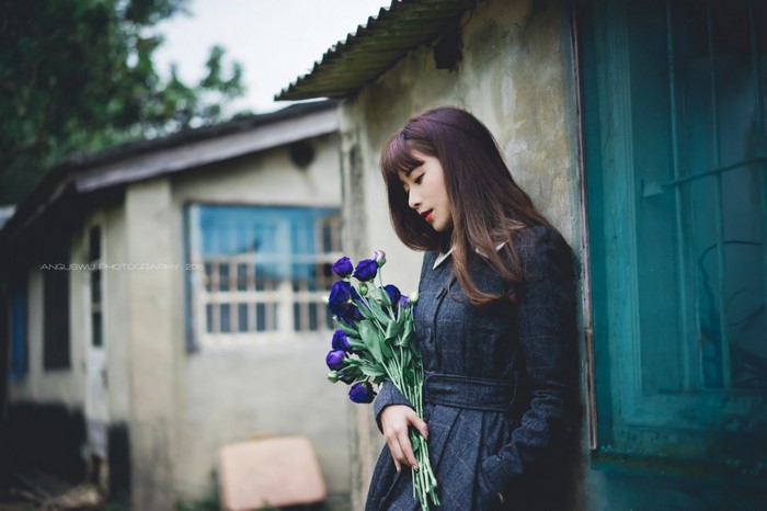 Woman holding a bouquet of purple flowers in front of a building