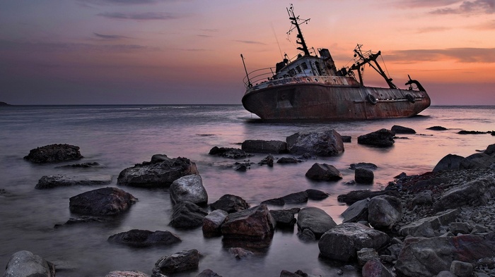 Shipwreck on rocky shore at sunset
