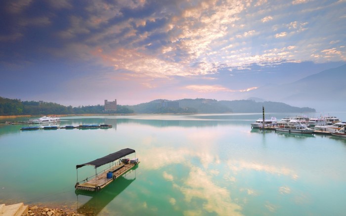 Boats on a calm lake with mountains and clouds at dawn