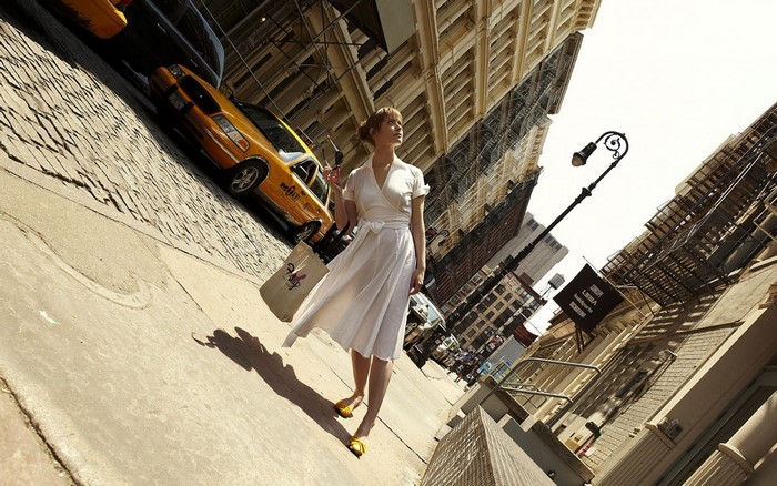 Woman in white dress walking on cobblestone street with yellow taxi