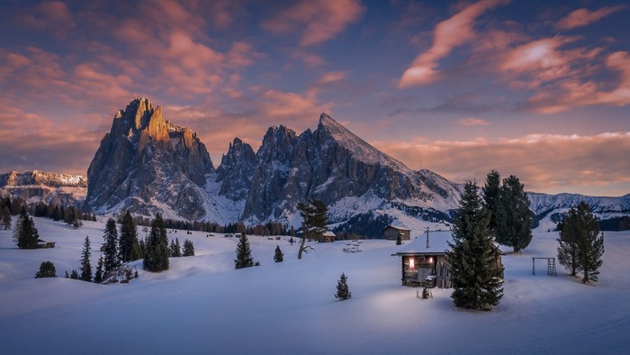 Snowy Dolomites mountains at sunset with cabins