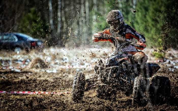 ATV rider covered in mud racing off-road