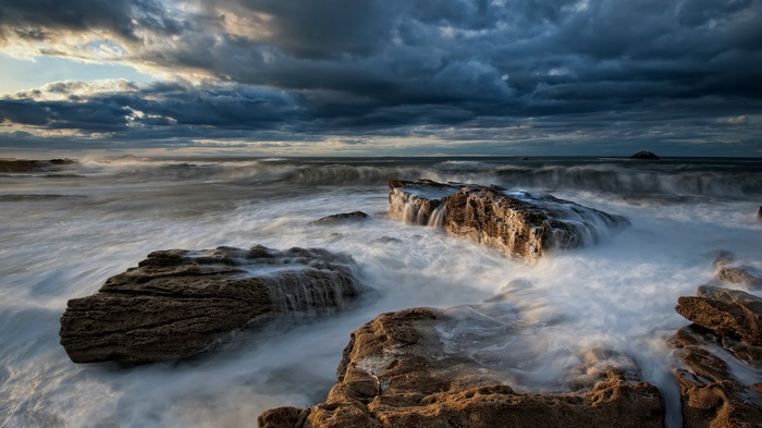 Waves crashing on rocks under stormy clouds