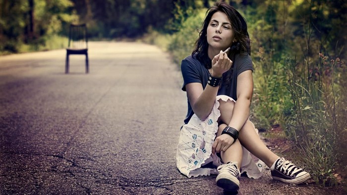 Woman sitting on road smoking a cigarette