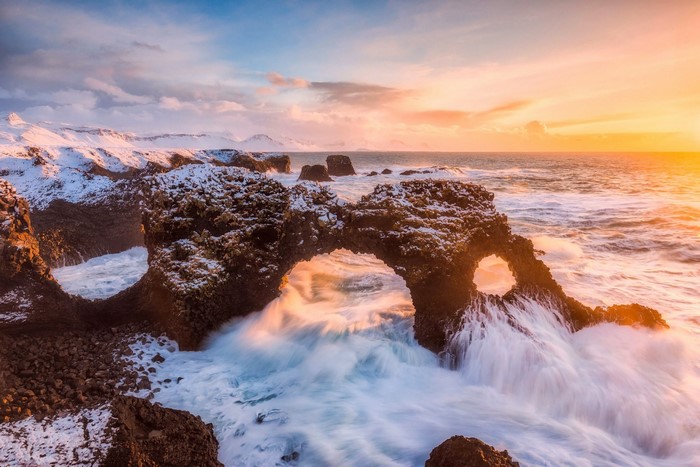 Waves crashing through rock arch at sunset in Iceland