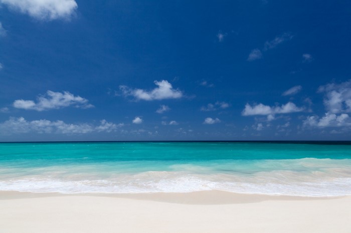 Turquoise ocean waves meet a white sand beach under a blue sky