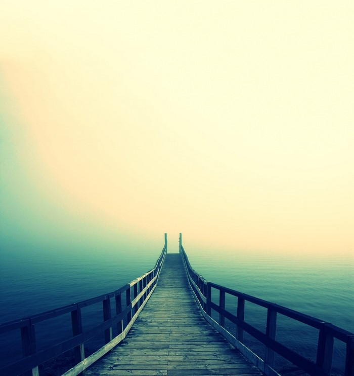 Wooden pier extending into misty ocean at dawn