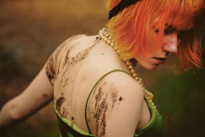 Woman with orange hair and pearl necklace covered in dirt