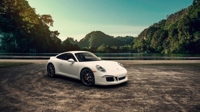 White Porsche 911 parked by a lake with mountains