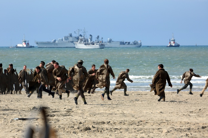 Soldiers running on a beach with ships in the background
