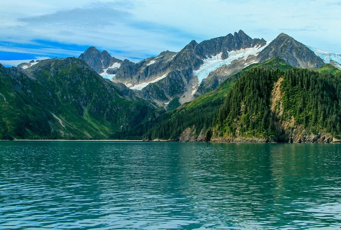 Turquoise water in front of green mountains and snowy peaks
