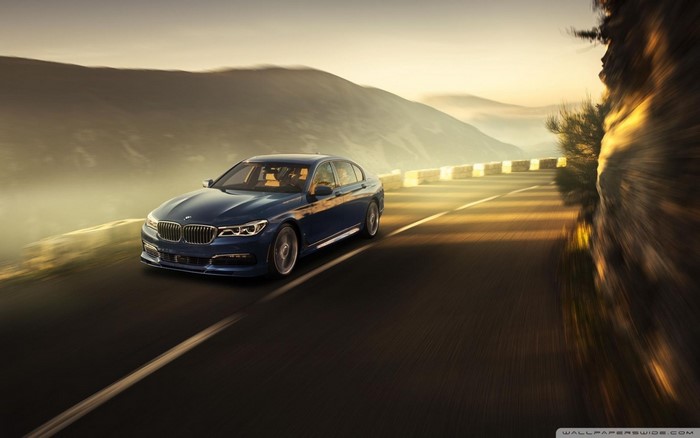 Blue Alpina B7 driving on a mountain road at sunset
