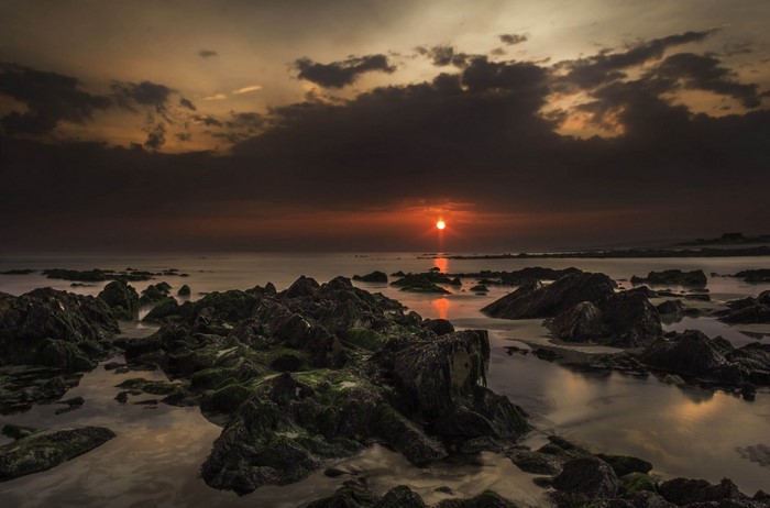 Sunset over rocky shore with ocean reflection