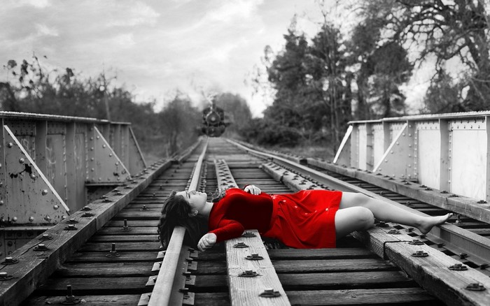 Woman in red dress lying on train tracks on a bridge