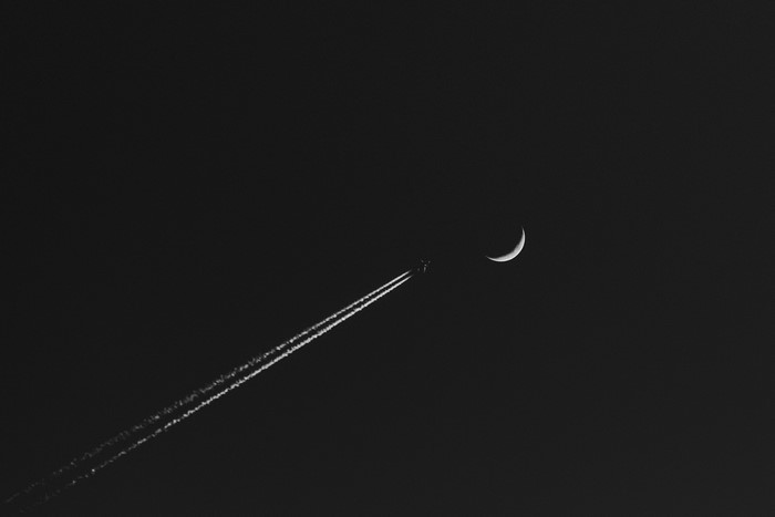 Airplane leaving contrails near a crescent moon