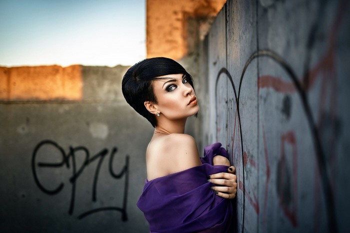 Woman with short black hair in purple dress against graffiti wall
