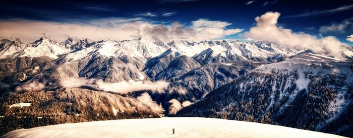 Snow-covered mountains and forests under a cloudy sky