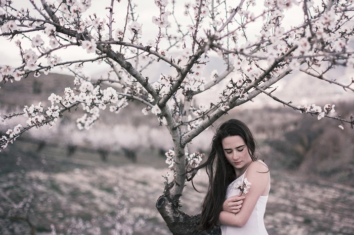 Woman in white dress holding a flower under a blooming tree