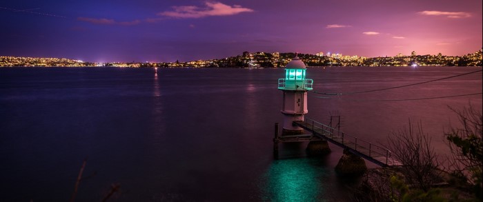 Lighthouse on the water at dusk with city lights
