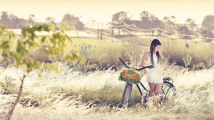 Woman in white dress with bicycle in a field