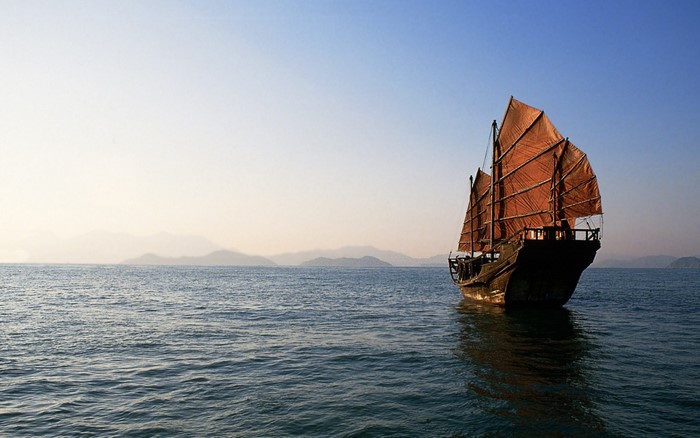 A Chinese junk sailing on the sea at sunset
