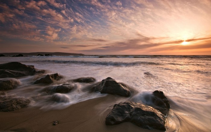 Sunset over the ocean with waves crashing on rocks
