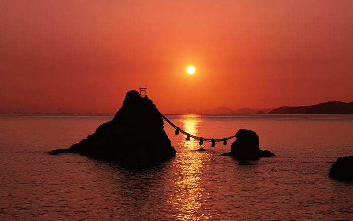 Sunset over the sea with a torii gate on a rock