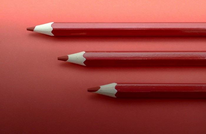 Three red colored pencils on a red background
