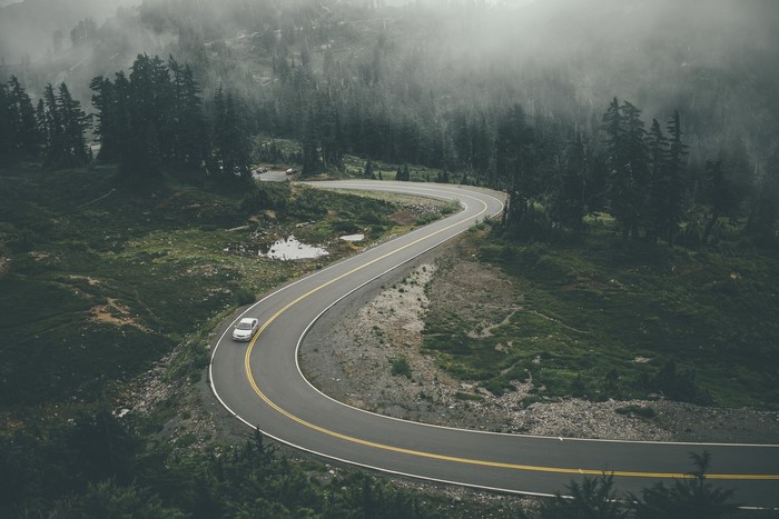 Winding mountain road with a car in foggy forest