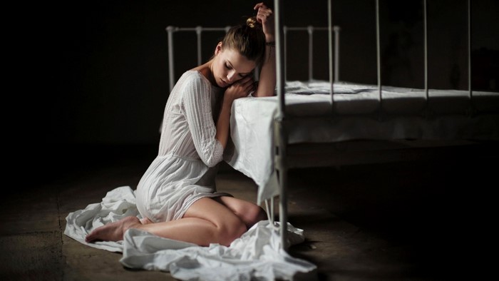 Woman in white dress sitting by a bed