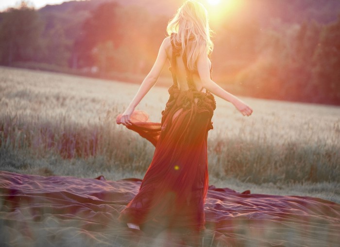Woman in red dress in a field at sunset