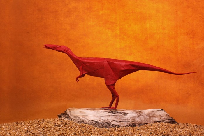 Red origami velociraptor on a log