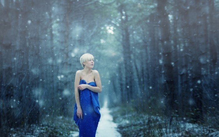 Woman wrapped in blue blanket in snowy forest