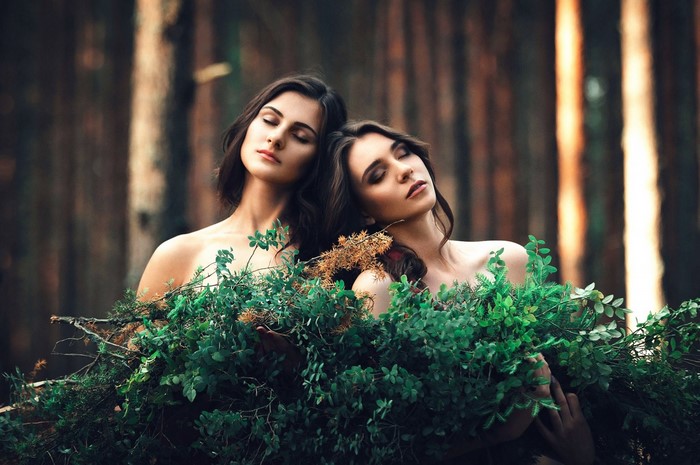 Two women with eyes closed in a forest surrounded by greenery