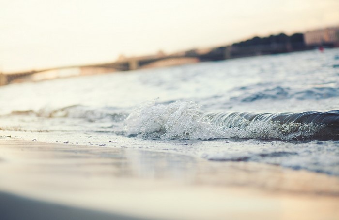 Wave crashing on a sandy shore with a bridge in the background