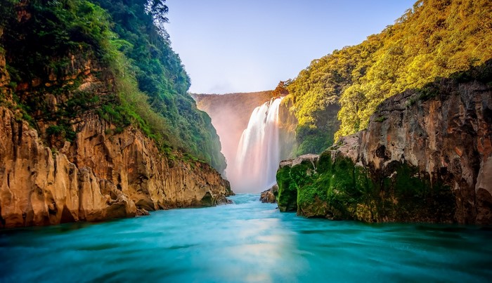 Waterfall cascading into a turquoise river between rocky cliffs