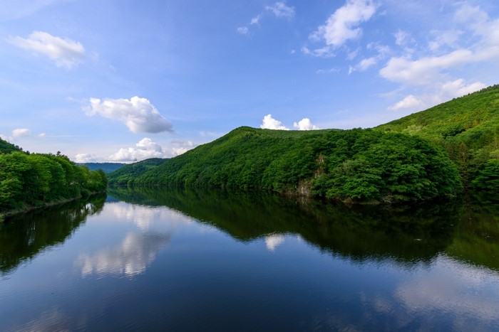 Green hills reflected in a calm lake under a cloudy sky