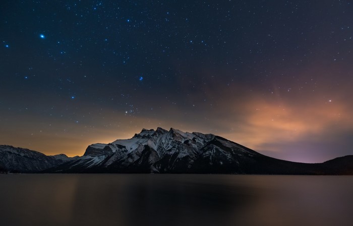 Snowy mountains reflected in a lake under a starry night sky