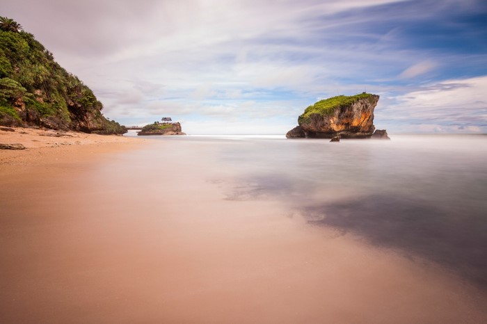 Long exposure beach with rock formations and a small building