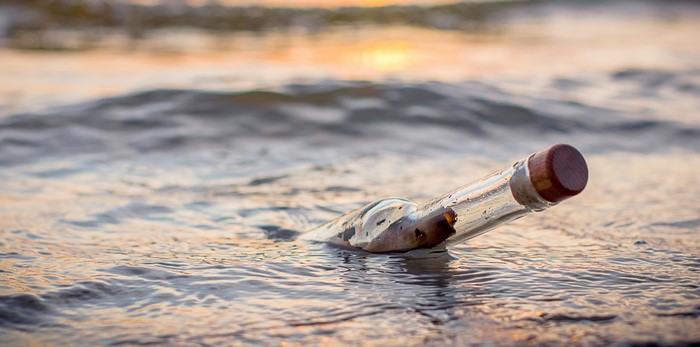 Message in a bottle floating in the sea at sunset