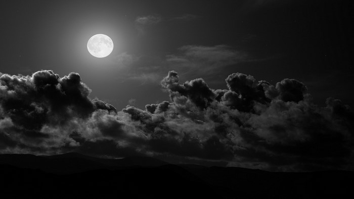 Full moon over dark clouds and hills