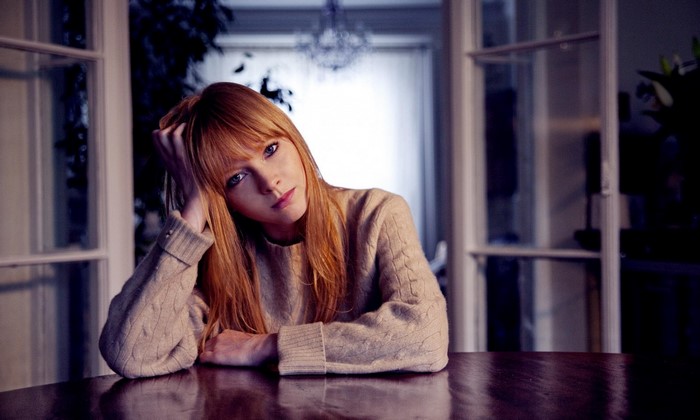 Lucy Rose, a redhead woman with blue eyes, sitting at a table
