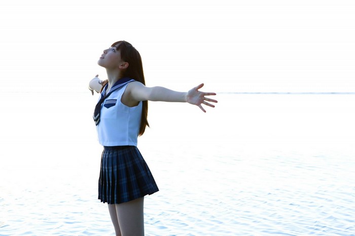 Young woman in sailor uniform with arms outstretched by the water