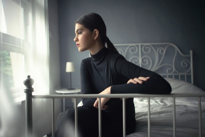 Woman in black turtleneck sitting on a bed