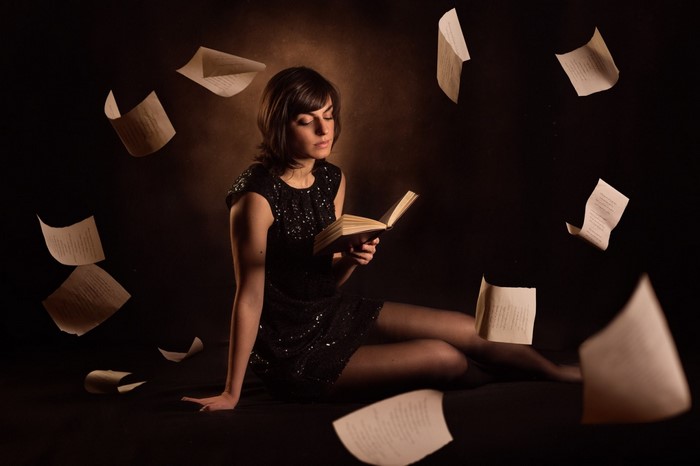 Woman in black dress reading a book with papers flying